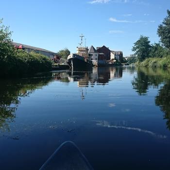 the view of a river under blue skies with green banks and a boat