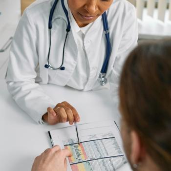 a woman in a white coat and stethoscope showing a document to a man